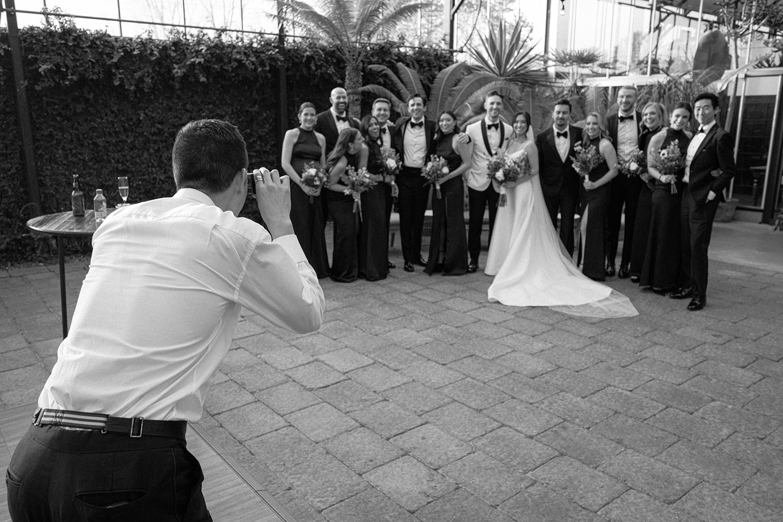 Candid film photo of a wedding guest taking a photo of the wedding party in black and white.