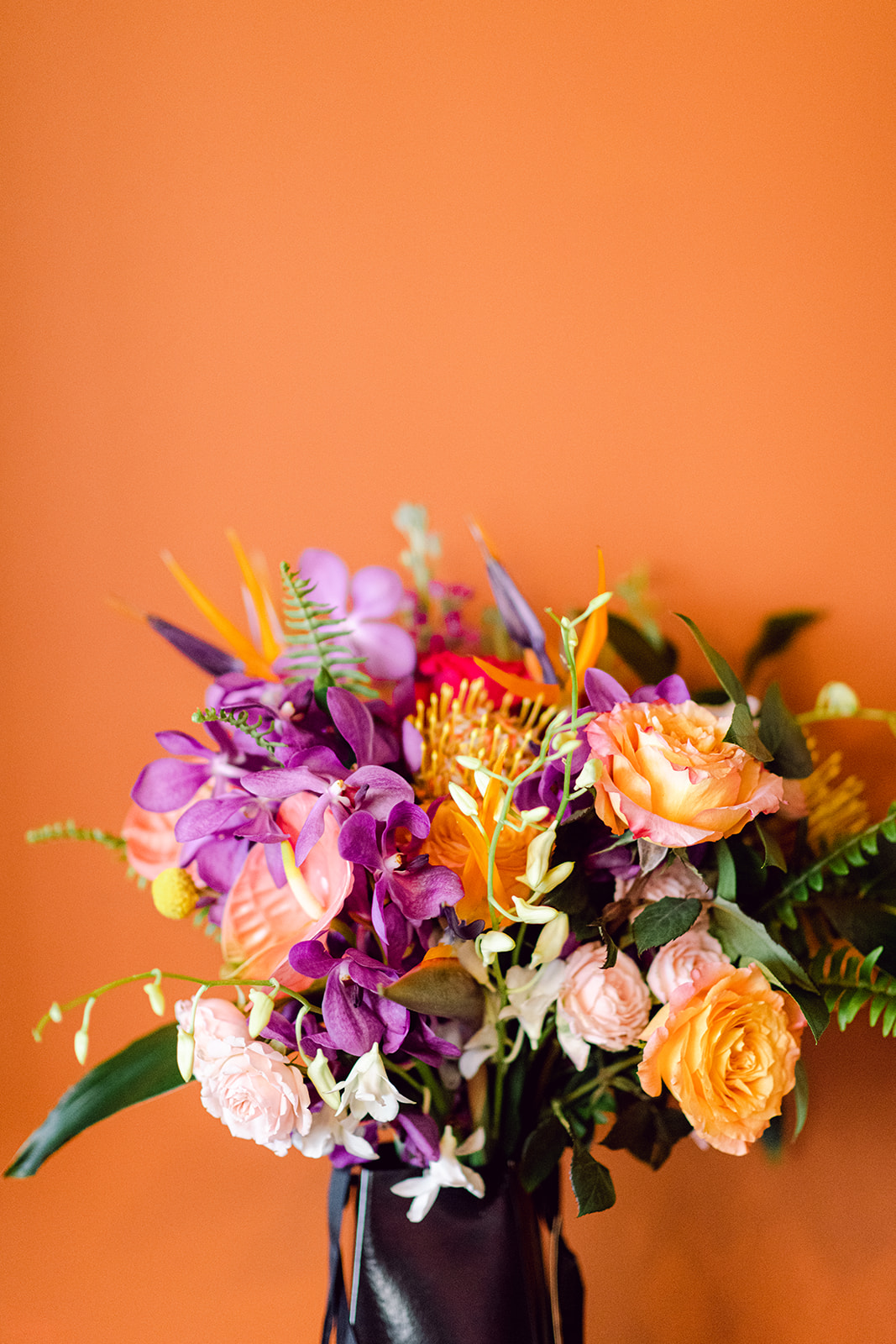 Brides colorful bouquet set against warm orange wall at Mayfair House Hotel & Garden in Miami on wedding day.