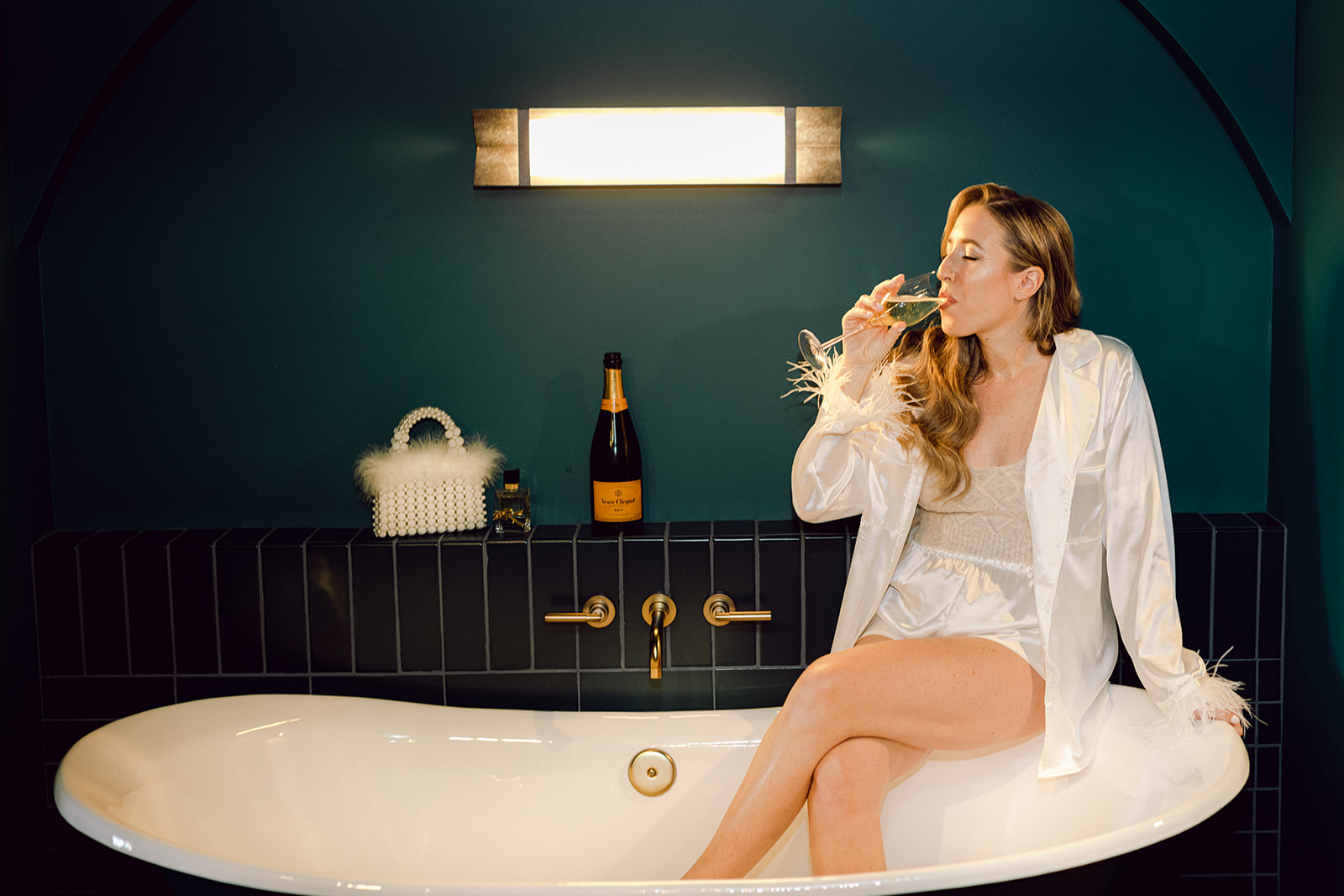 Bride drinking glass of champagne in clawfoot tub at Mayfair House Hotel & Garden in Miami on her wedding day.