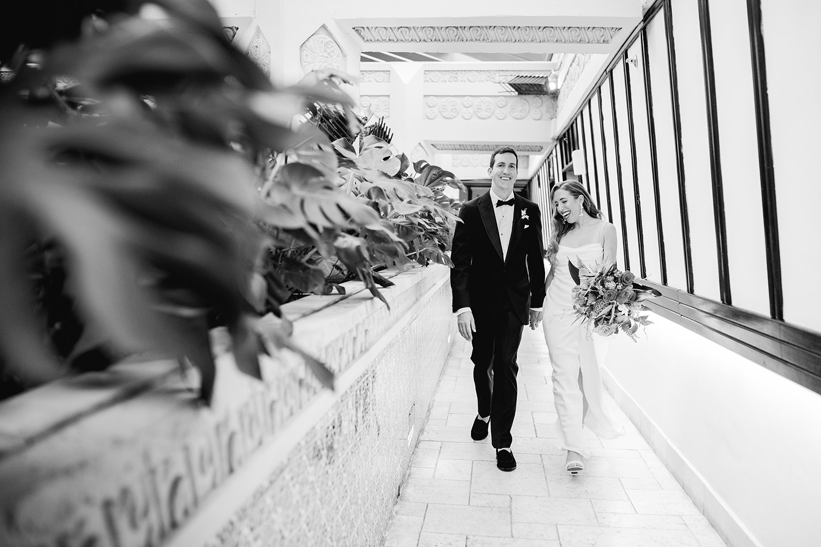 Black and white bride & groom walking hand in hand down hallway at Mayfair House Hotel & Garden in Miami on wedding day.