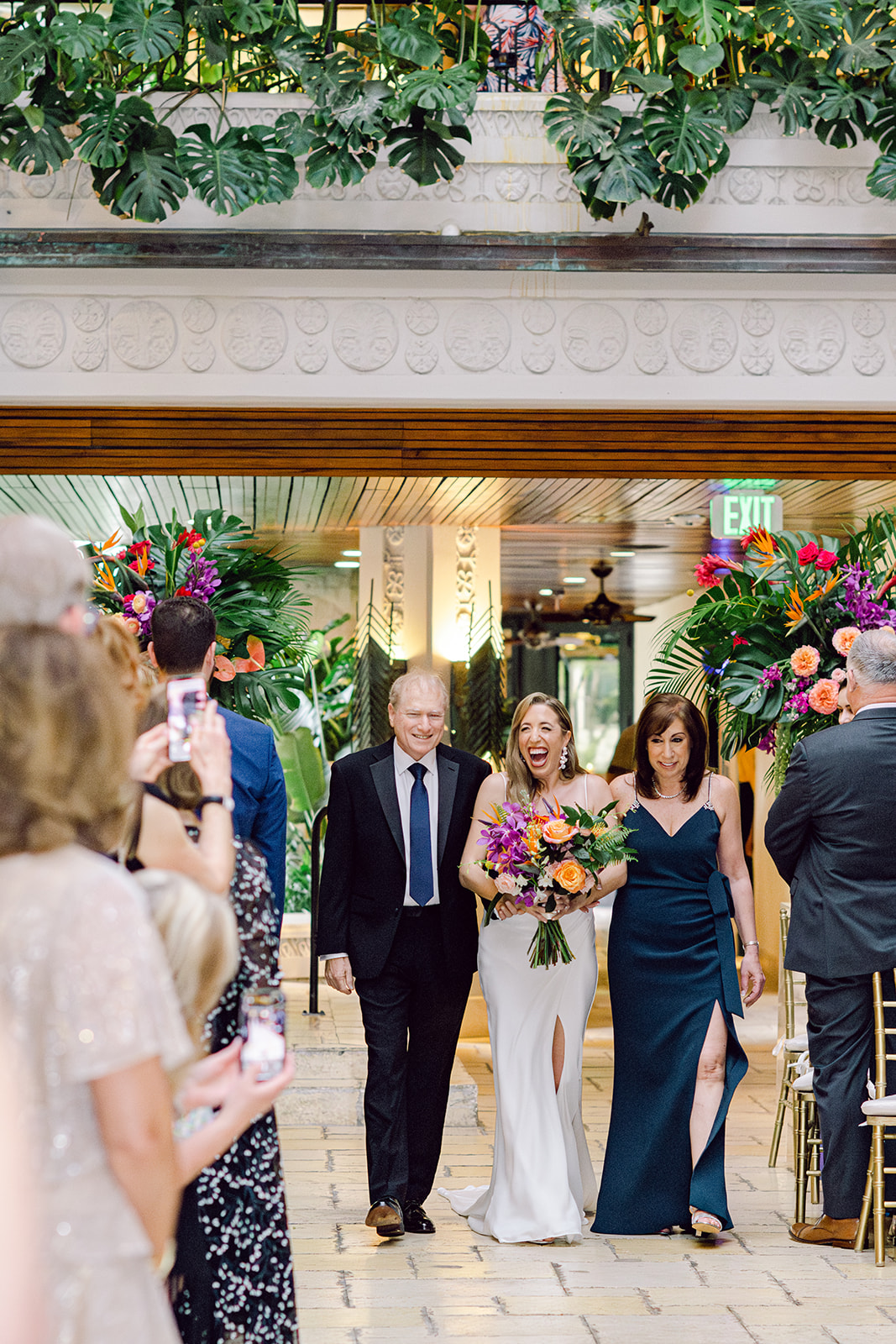 Bride with parents walk down aisle at ceremony at Mayfair House Hotel & Garden in Miami on wedding day.