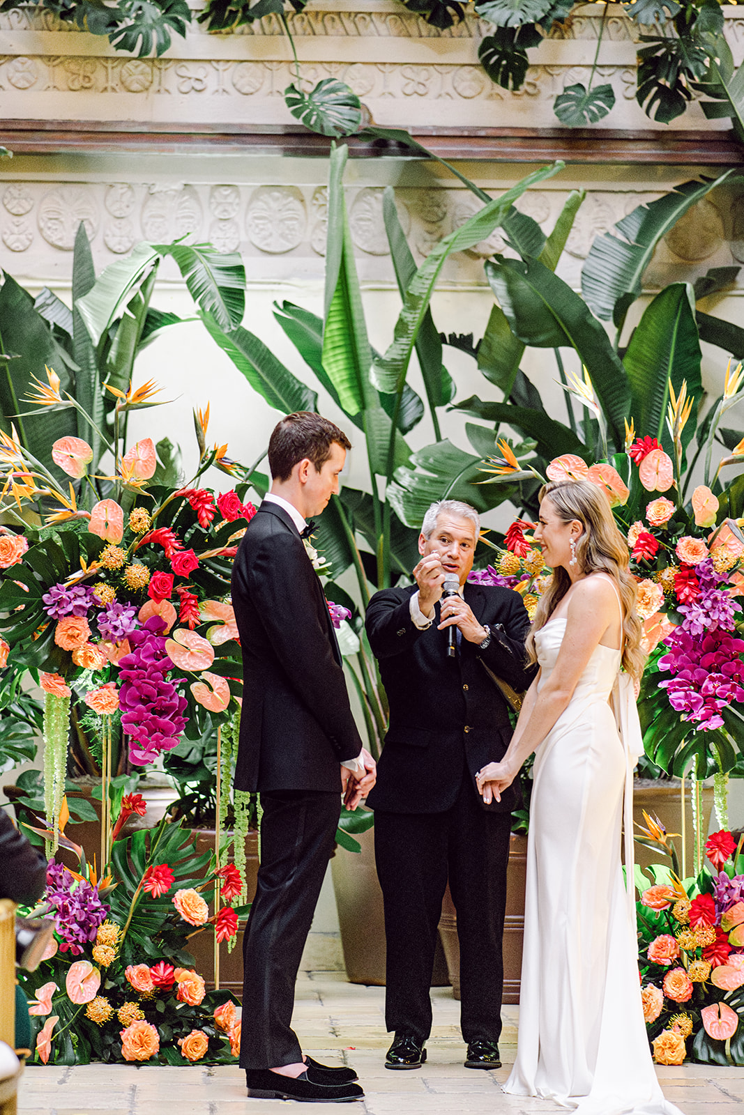 Officiant holds up rings at the floral altar during ceremony at Mayfair House Hotel & Garden in Miami on wedding day.