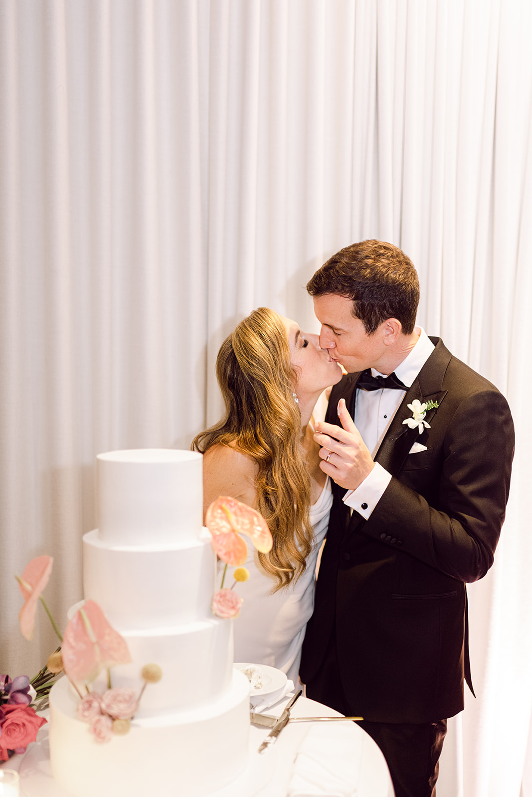 Bride and groom kiss after cutting cake in reception hall of Mayfair House Hotel & Garden, Miami on wedding day.