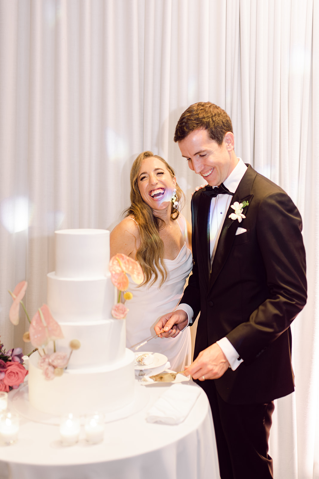 Colorful smiling bride and groom cutting cake in reception hall of Mayfair House Hotel & Garden, Miami on wedding day.
