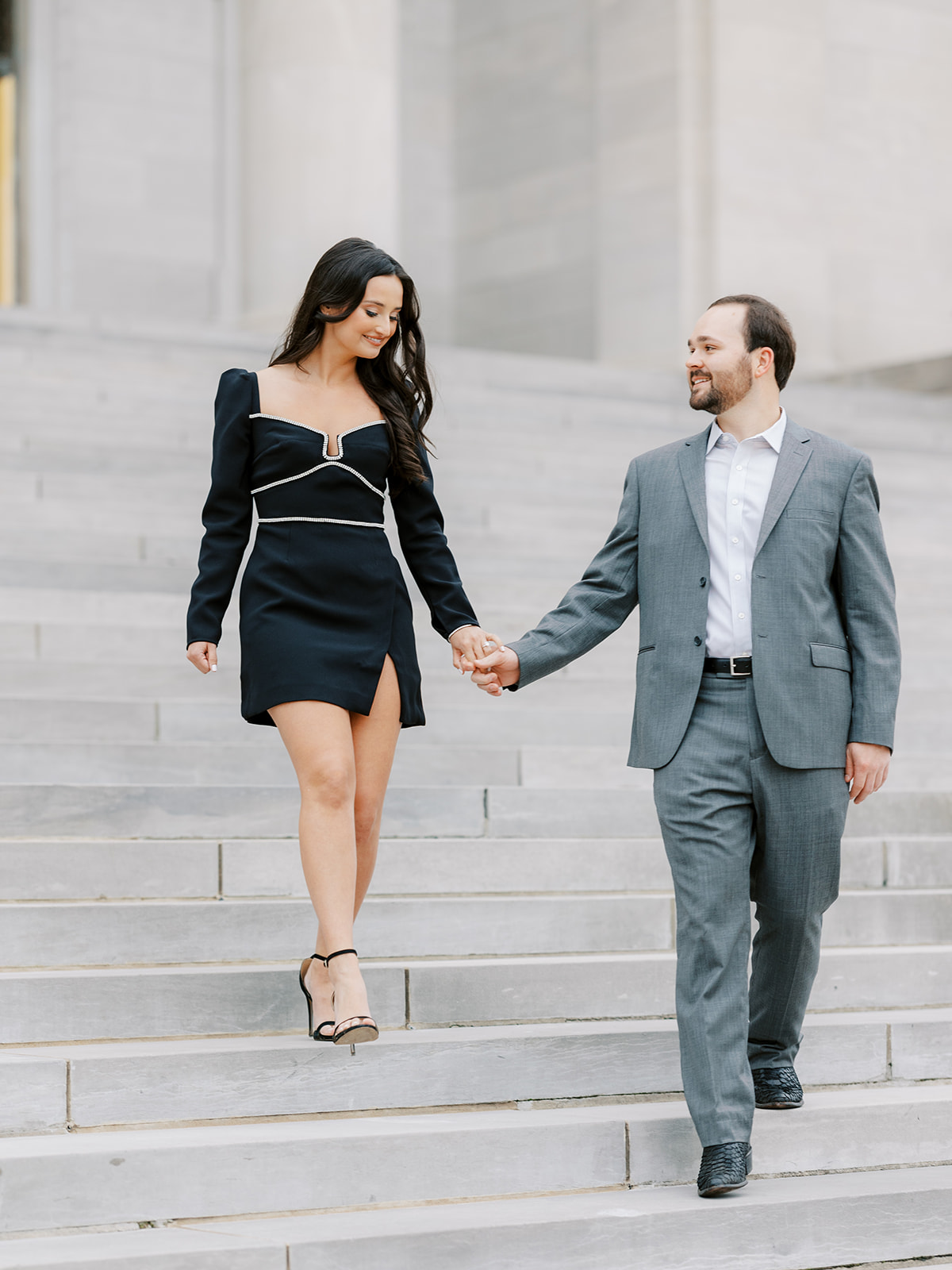 Couple in dressy outfits walk down the steps of the Arkansas State Capitol together