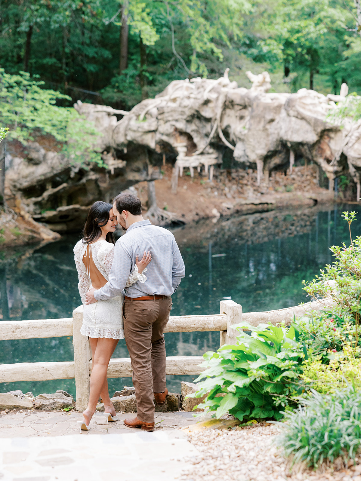 Couple stands together and faces away from the camera towards the water