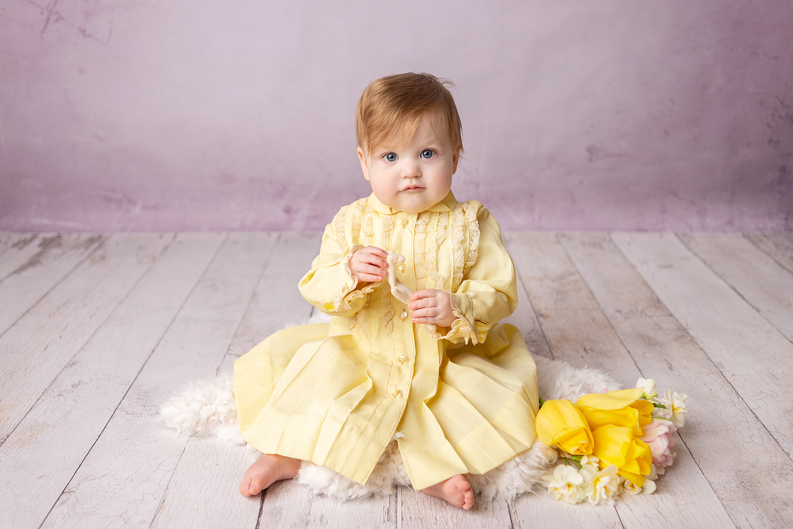 A one year old baby girl milestone session with a purple backdrop and a yellow family heirloom dress