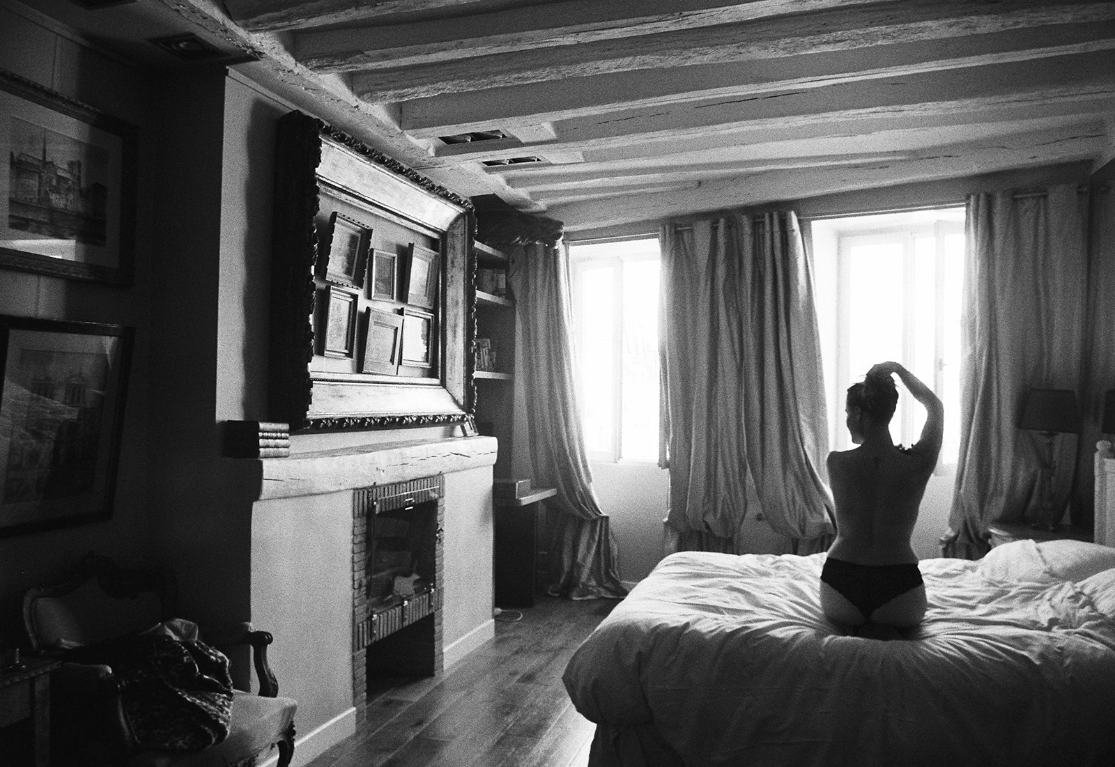 Black and white photo of woman sitting on a bed with her back to the camera in an apartment in Paris