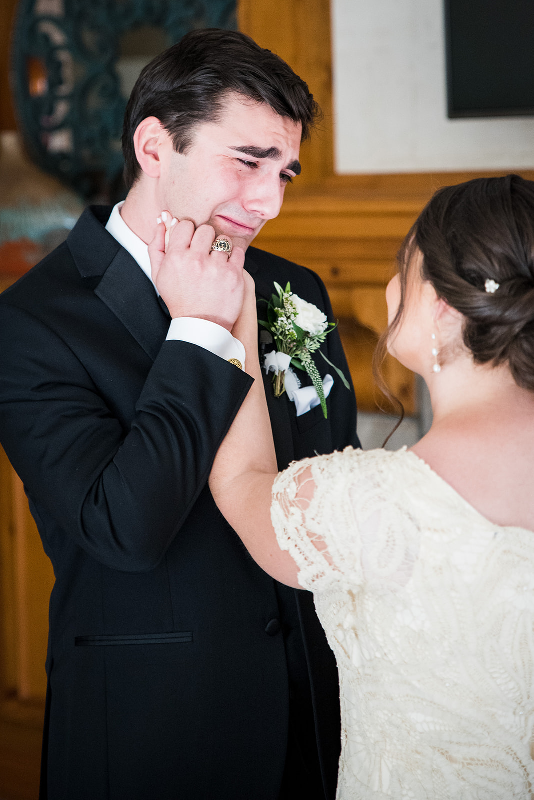 Groom holds bride's hand close to his face as she wipes a tear from his eye.