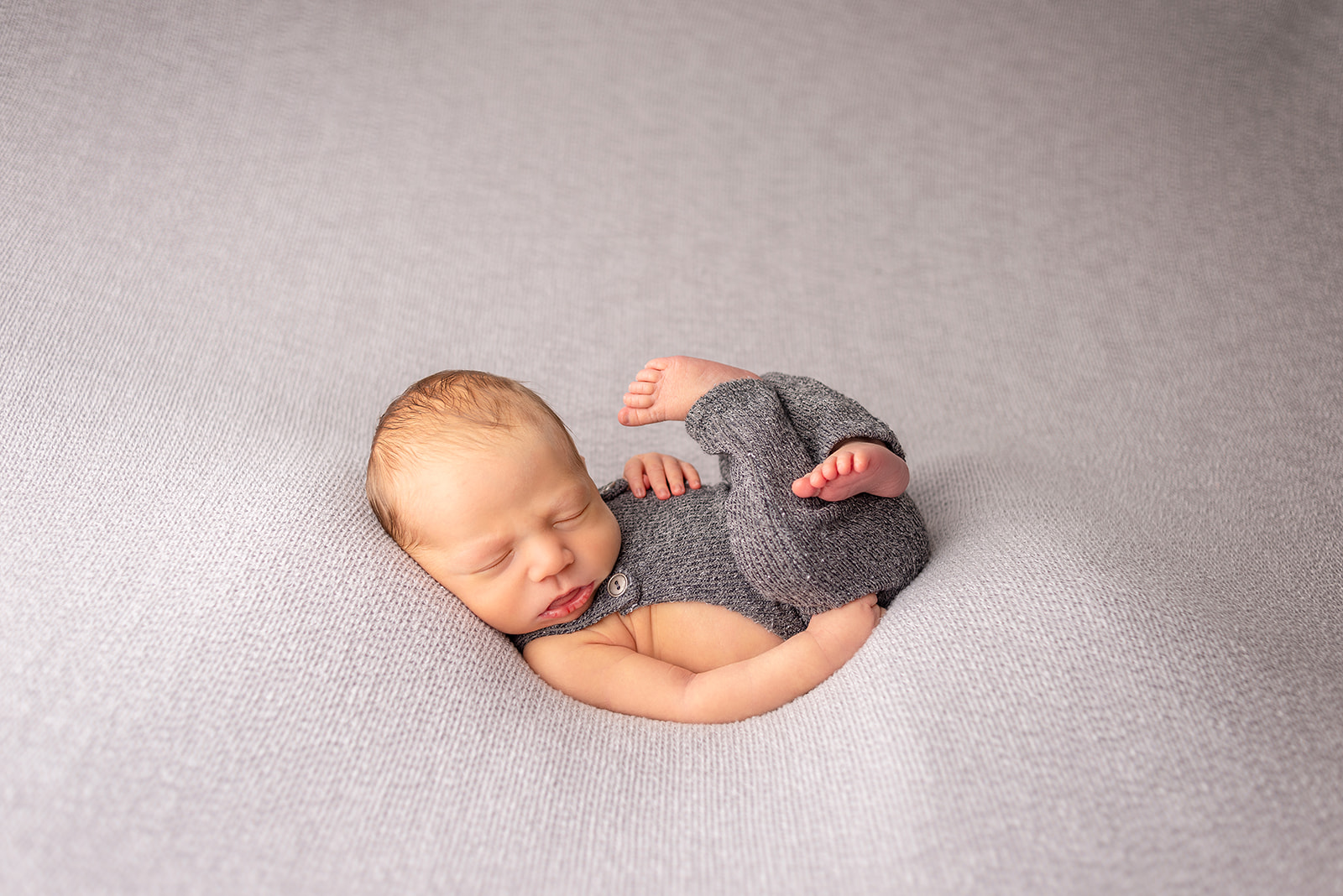 A sleeping newborn boy in Celesta Champagne Photography studio in a dark gray onesie upon a gray blanket