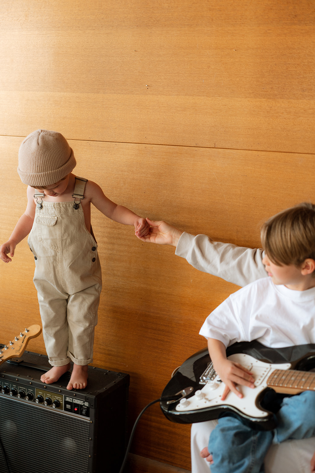 toddler stands on amp while brother plays guitar