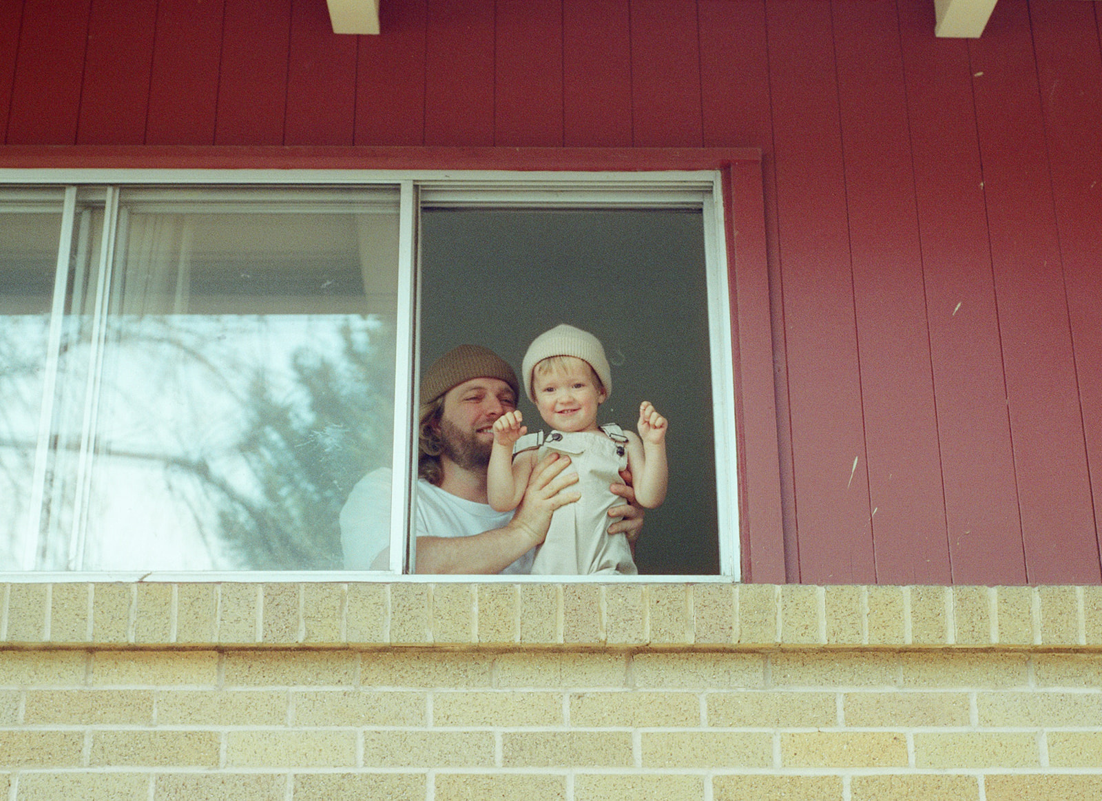 Film portrait of dad holding little boy in window of the house