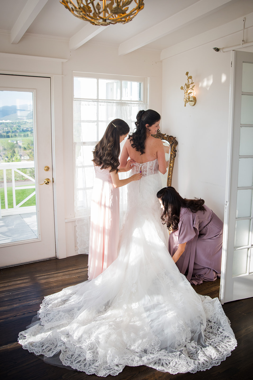 Bride's sister and mother attend to her wedding dress and help her get ready.