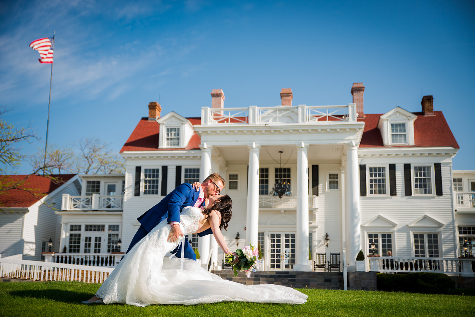 Groom dips bride for a kiss in front of the grand Manor House venue.
