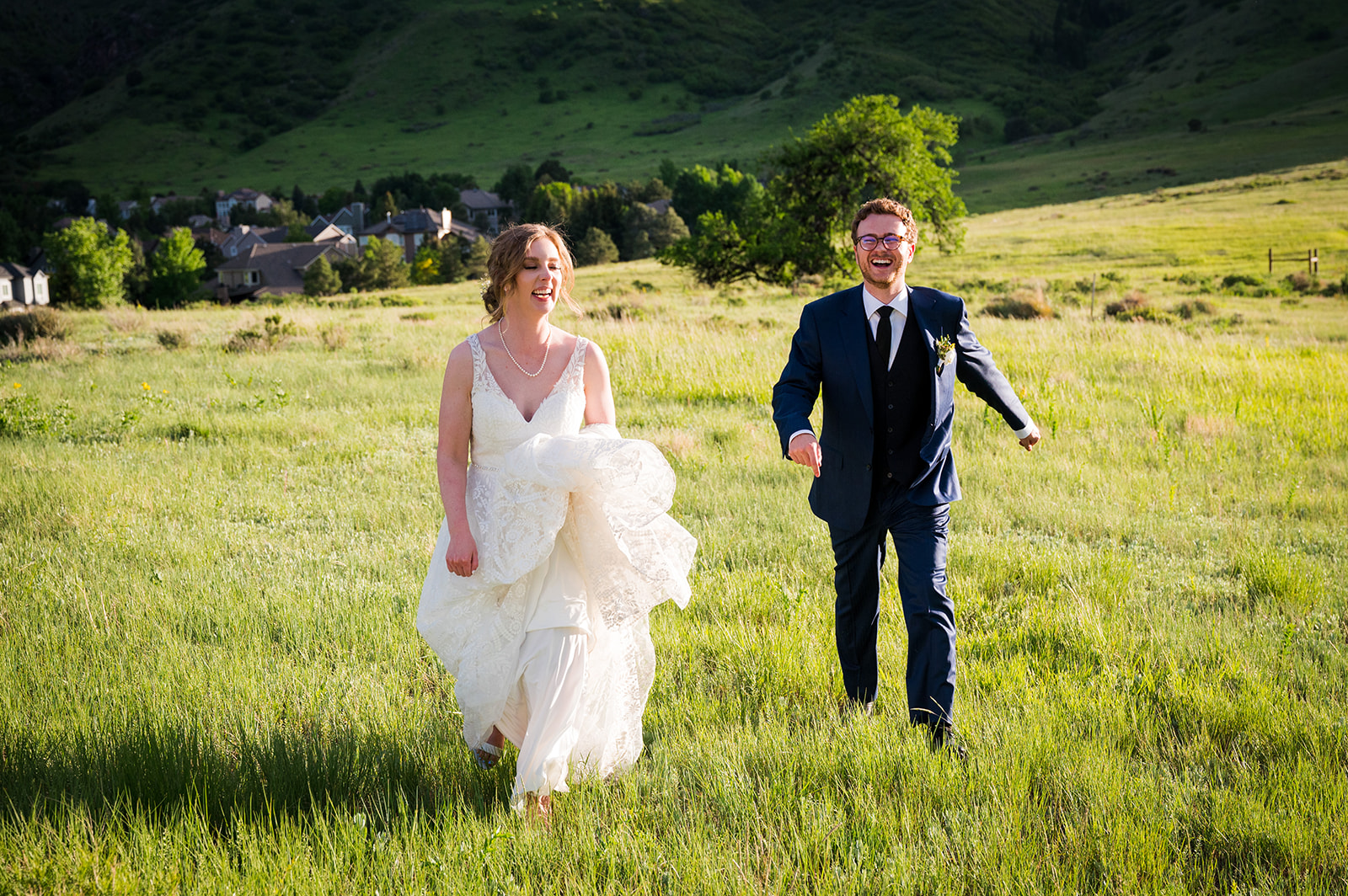 Bride and groom run through field laughing at golden hour.