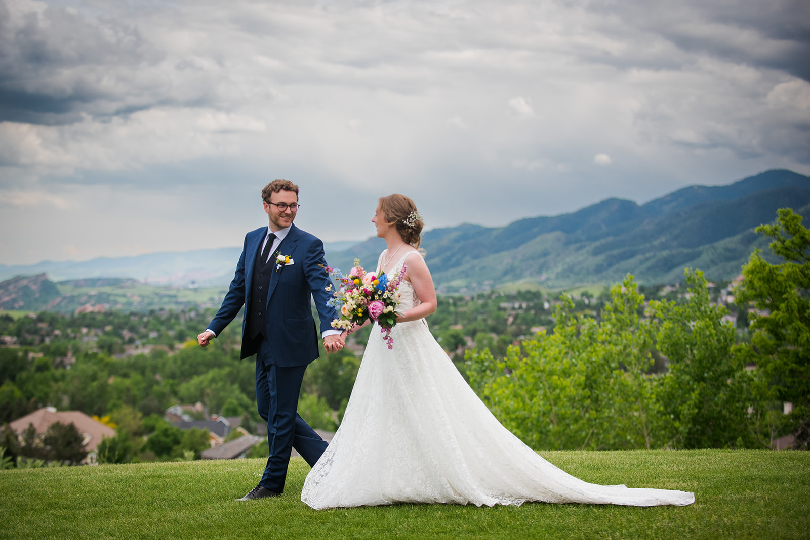 Groom leads bride across a field with scenic Colorado landscape in the background.