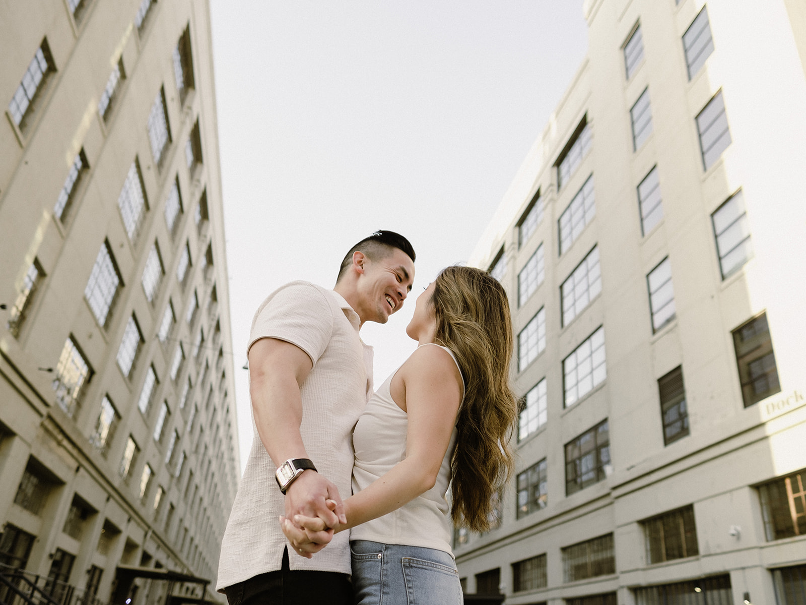 An engaged couple dances with buildings behind them.