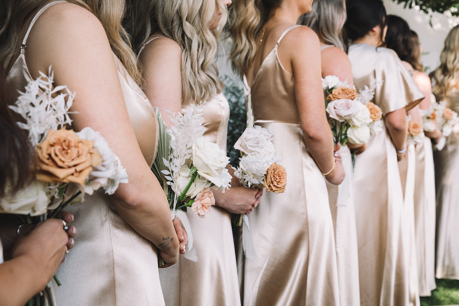 Bridesmaids wear neutral dresses and hold neutral floral bouquets. 
