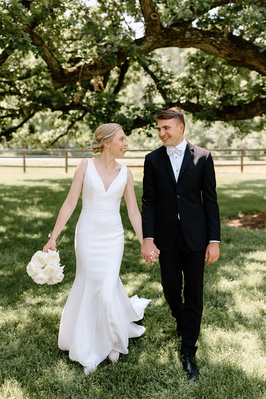 Bride and groom hold hands and walk under a tree