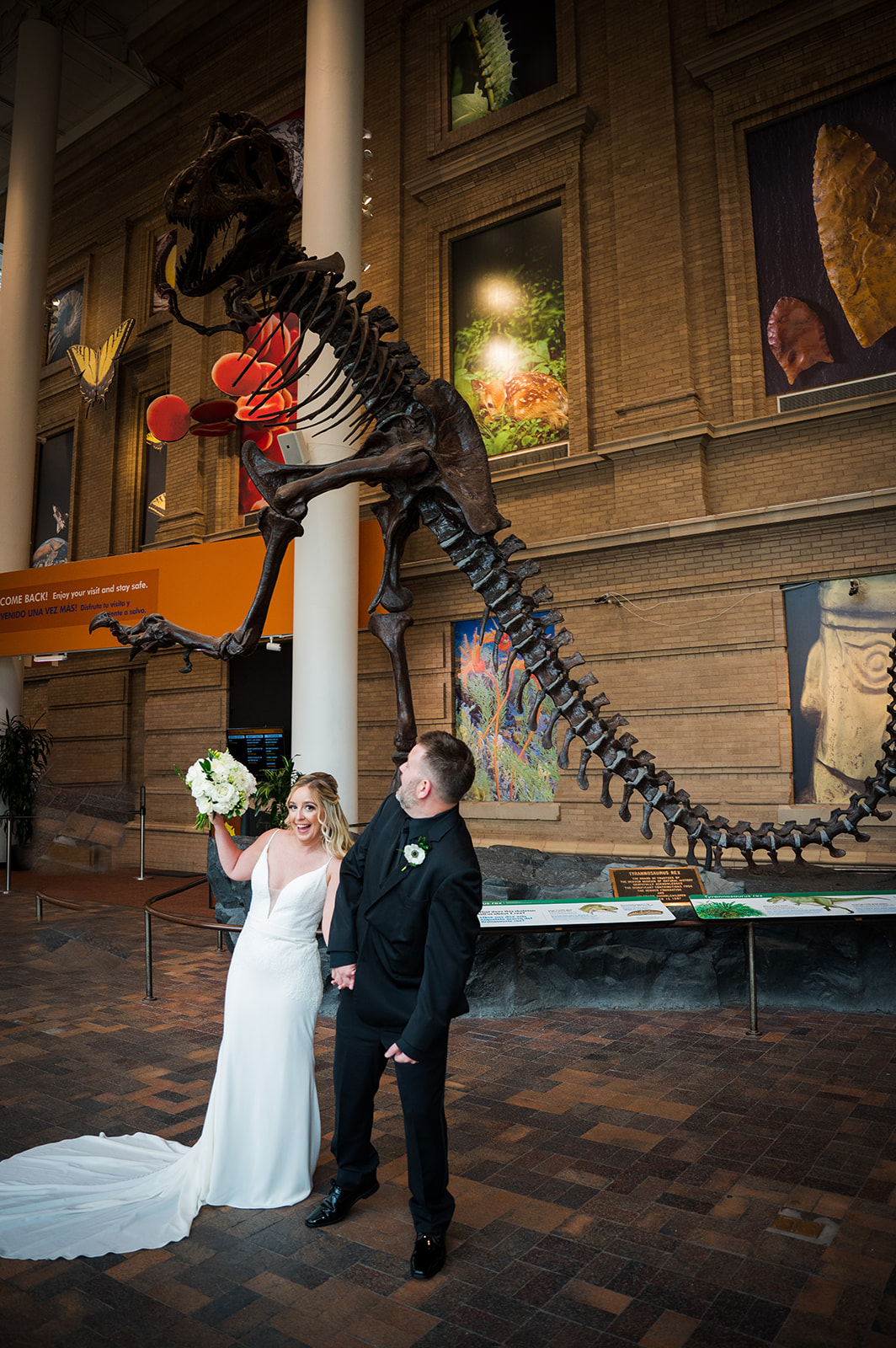 Bride and groom act silly in front of large dinosaur skeleton at the Denver Museum of Nature and Science.
