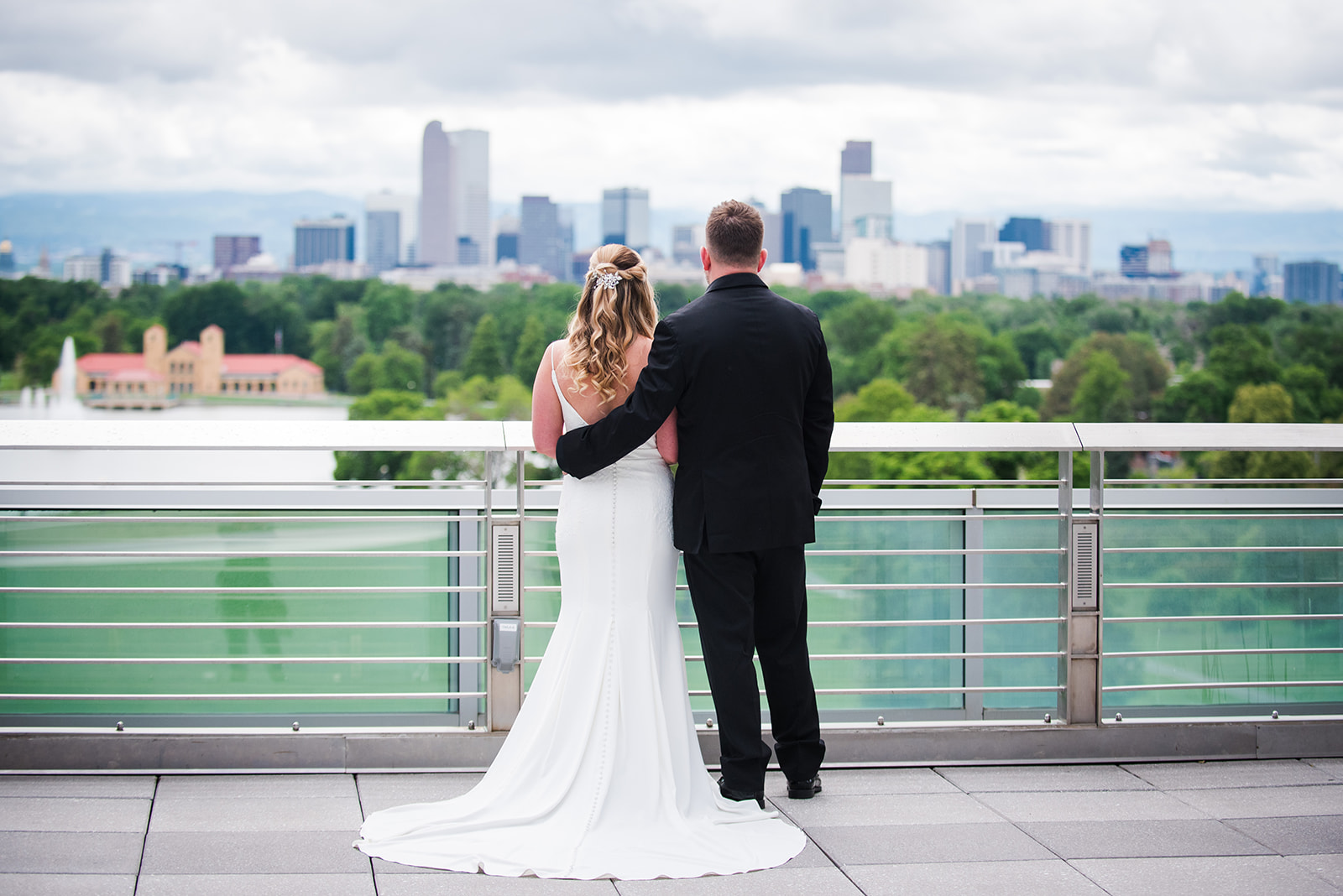 Bride and groom stand on rooftop and stare out over the Denver city skyline.