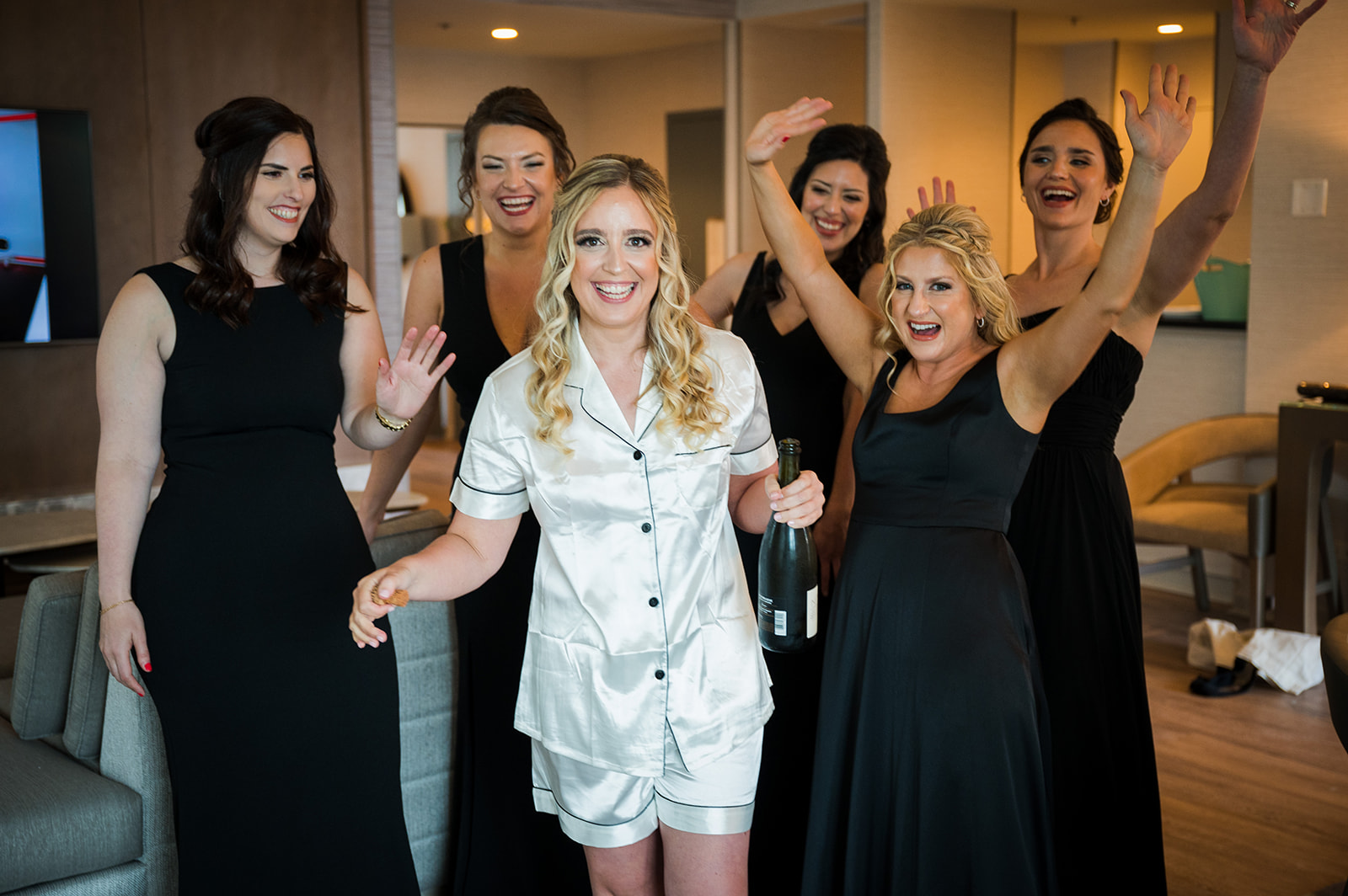 Bride holds a bottle of champagne surrounded by her bridesmaids who are celebrating