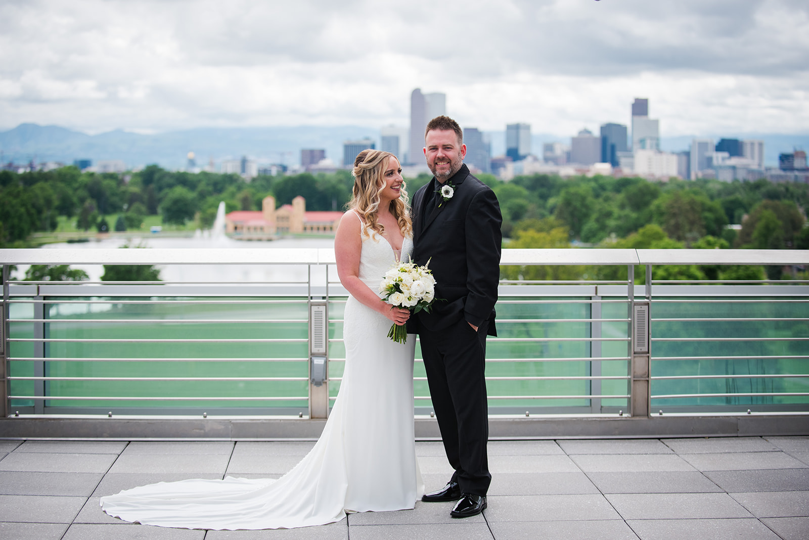 Groom smiles at the camera as bride looks up at him with Denver city skyline in the background.