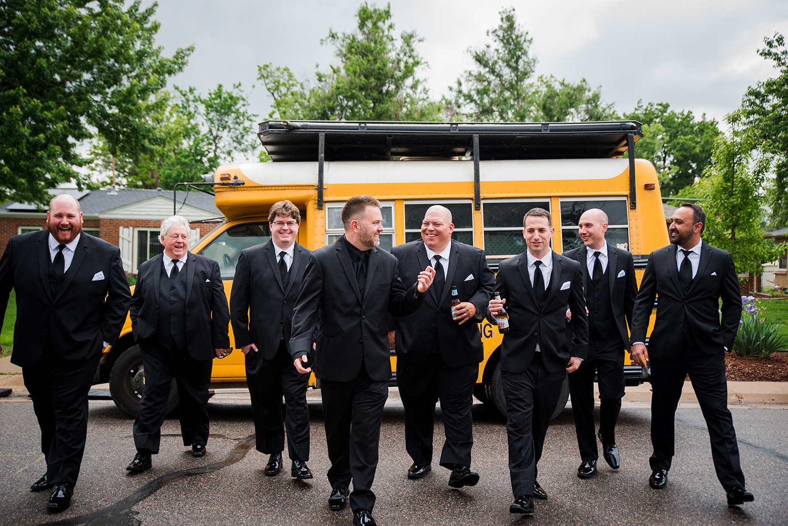 Groomsmen walk and talk with each other with school bus in the background.
