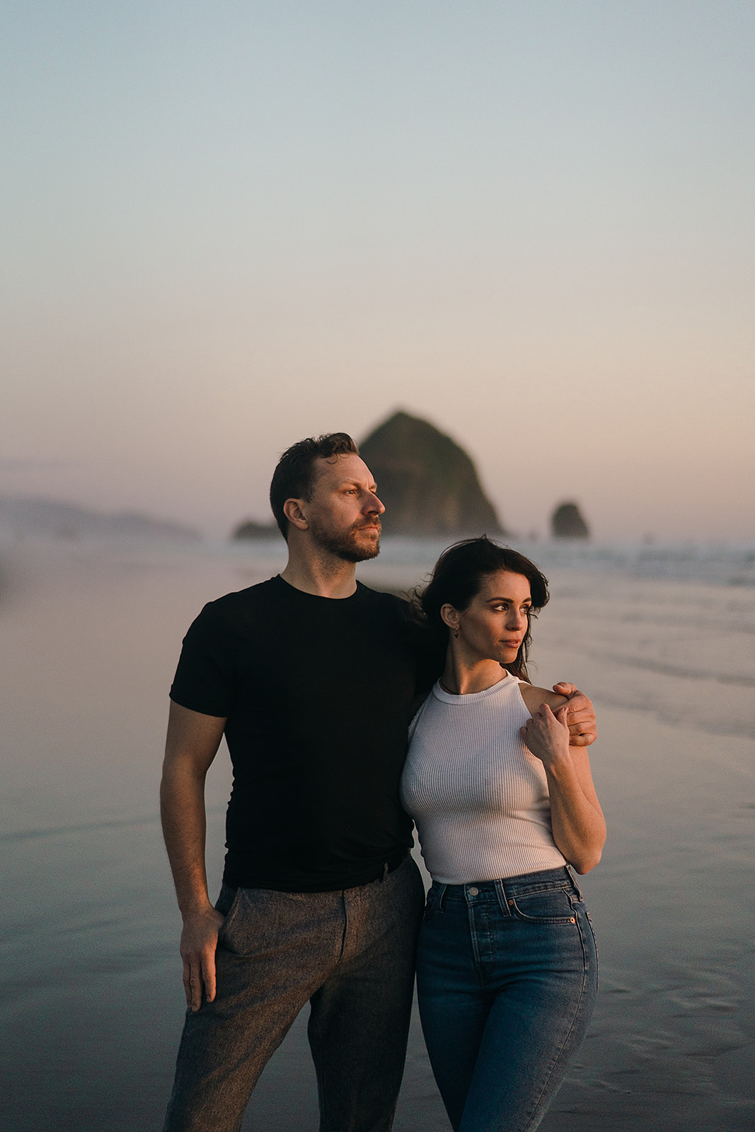 couple poses for couples portraits in front of haystack rock during Cannon Beach Engagement session