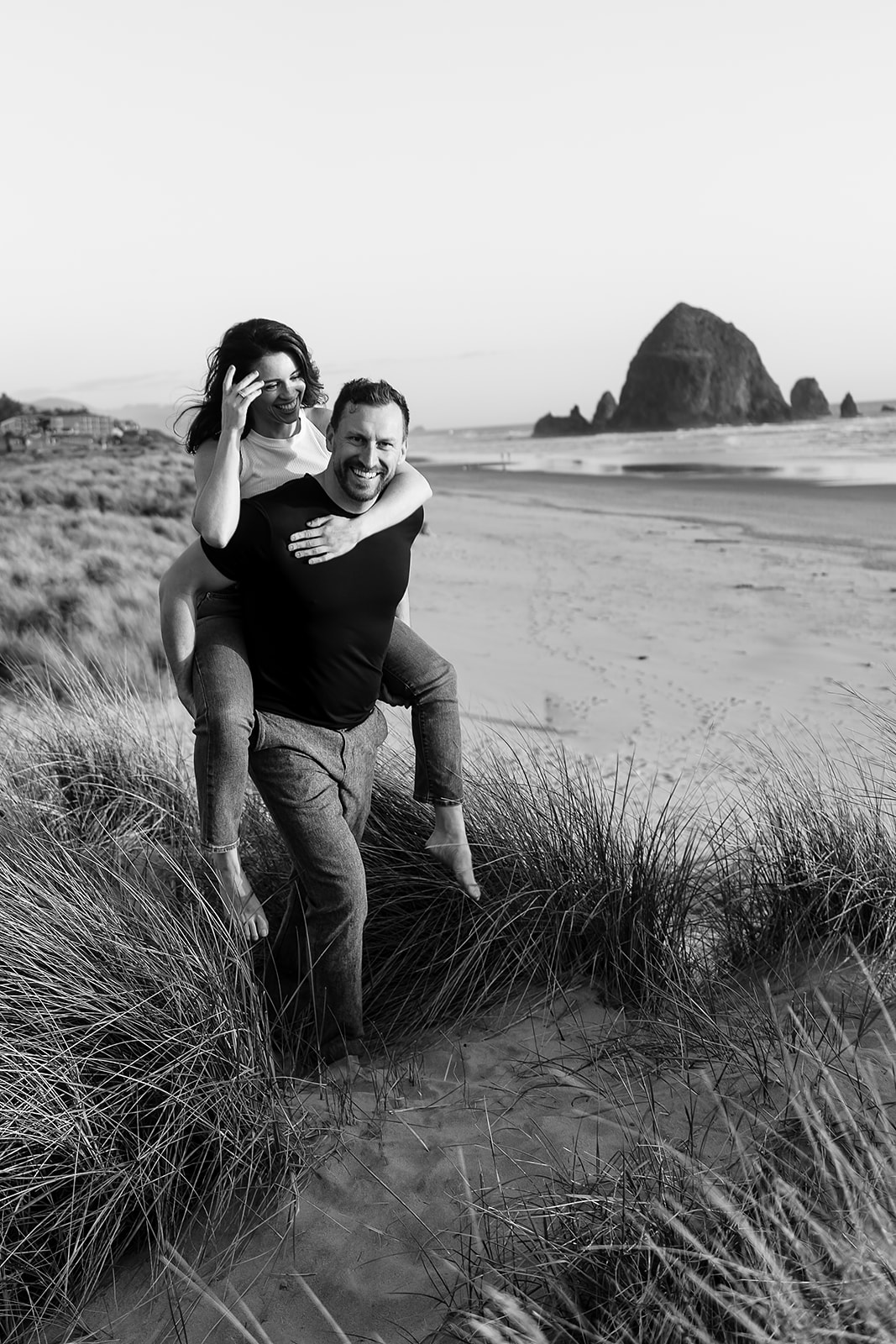 couple climbs over beach grass on the sand dunes during Cannon beach couples portrait session