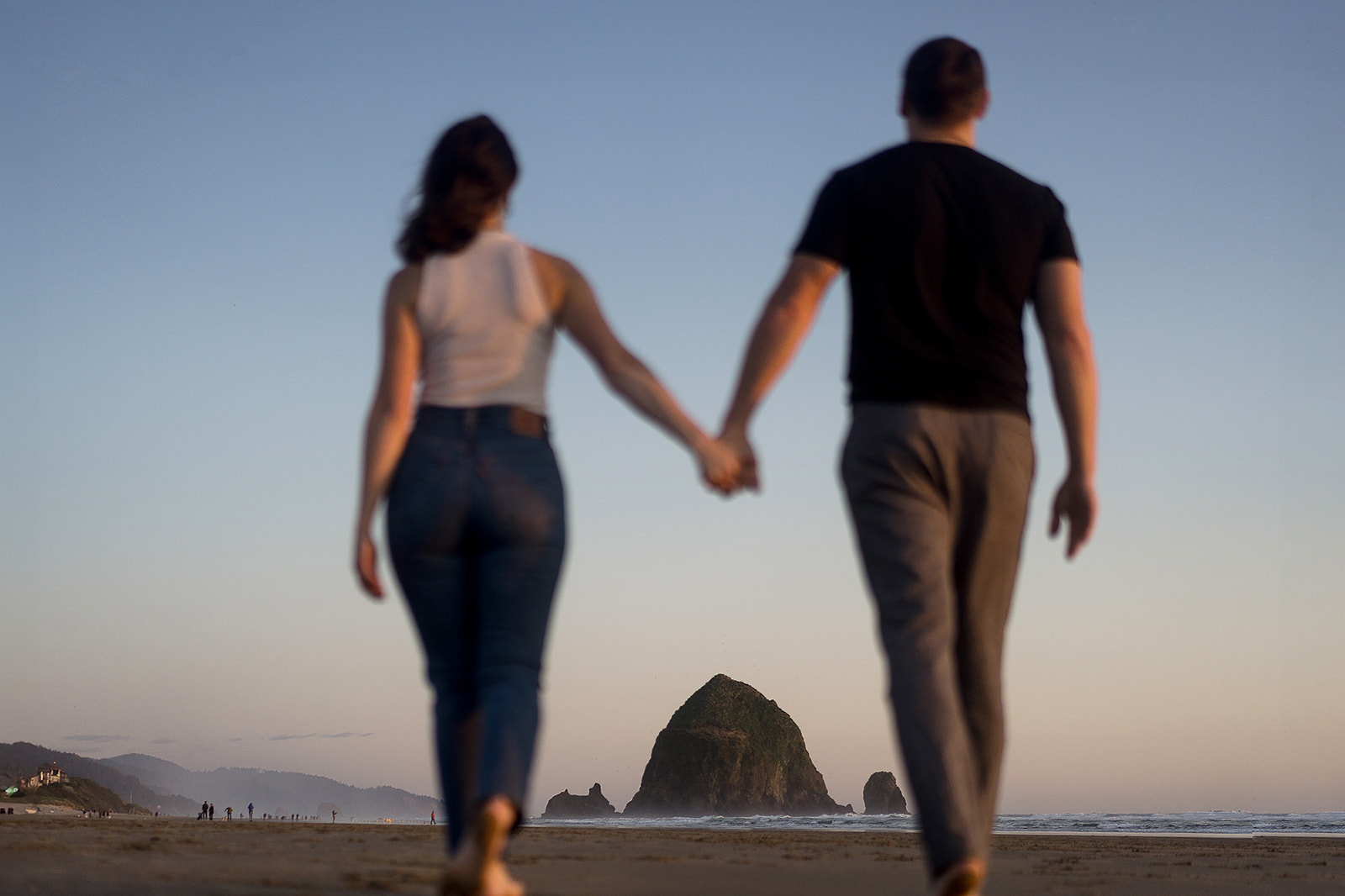 Couples walks toward Haystack Rock during engagement session