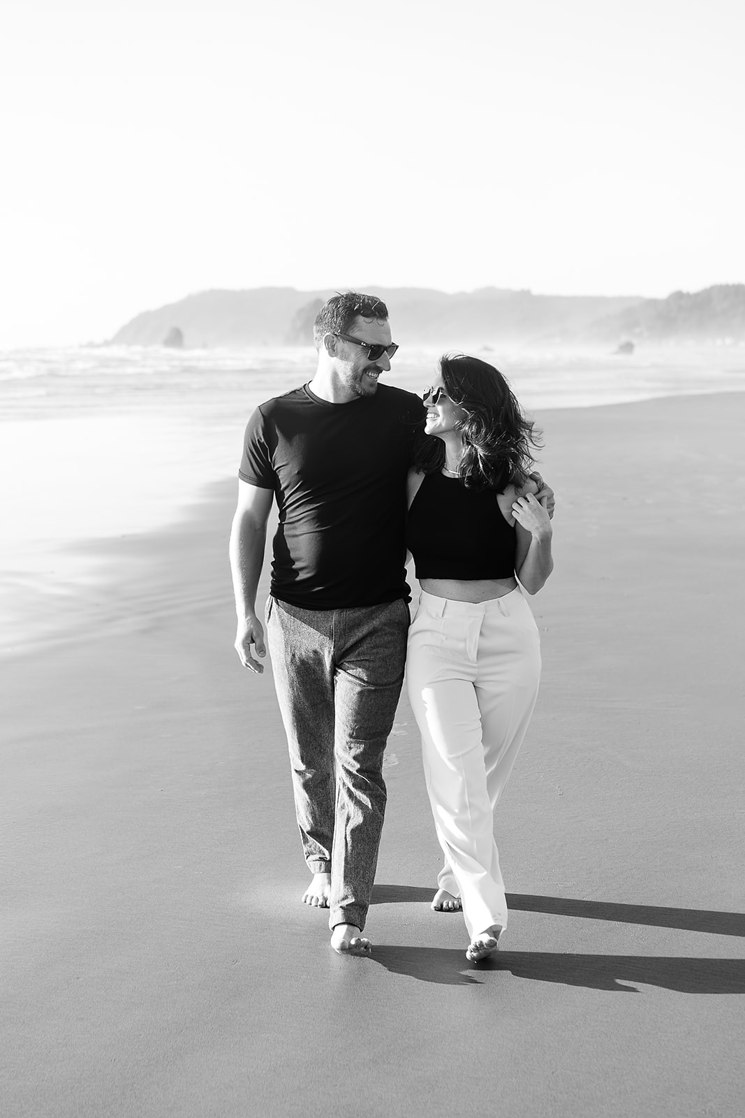 couples walks along cannon beach with arms around each other during engagement session