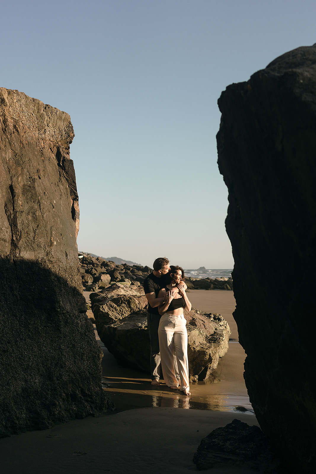 couple poses between large rock formations on the Oregon Coast for Cannon beach couples portrait session