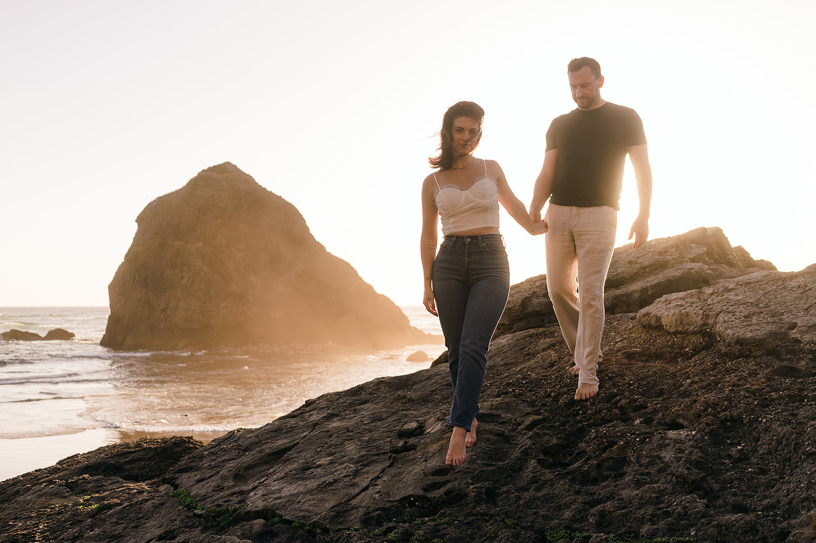 Couple walks along rock formation at secret beach during Cannon beach couples portrait session