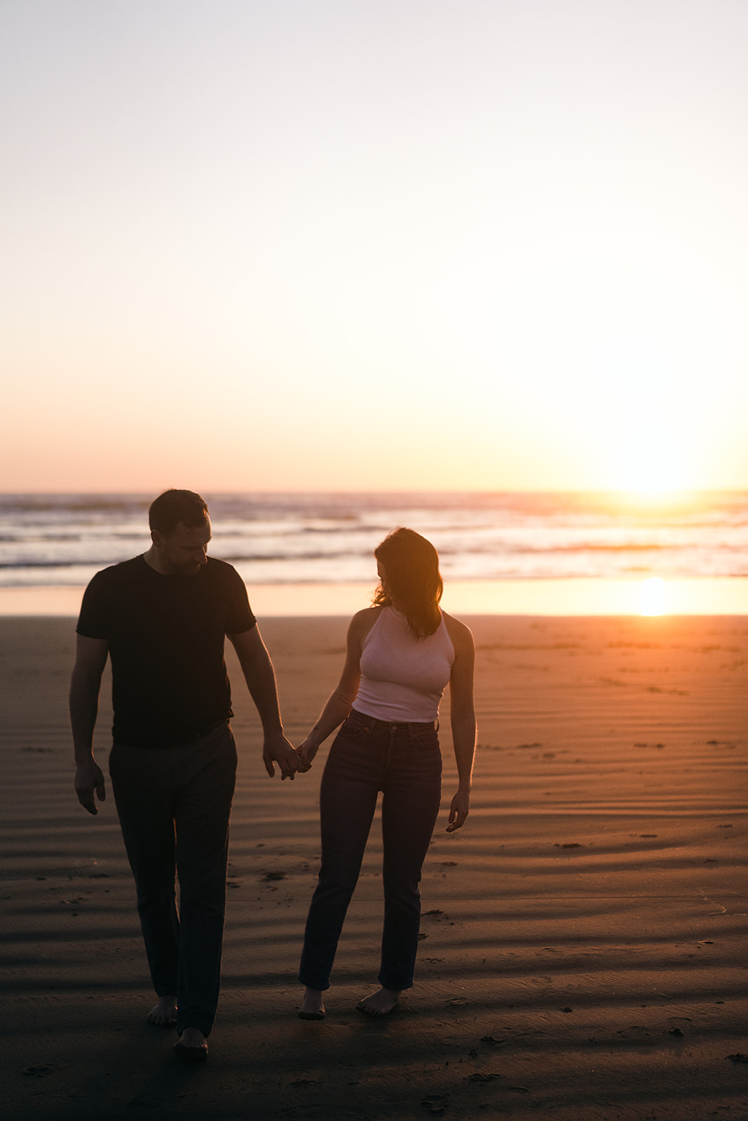 sunset engagement session with couple walking along the wet sand