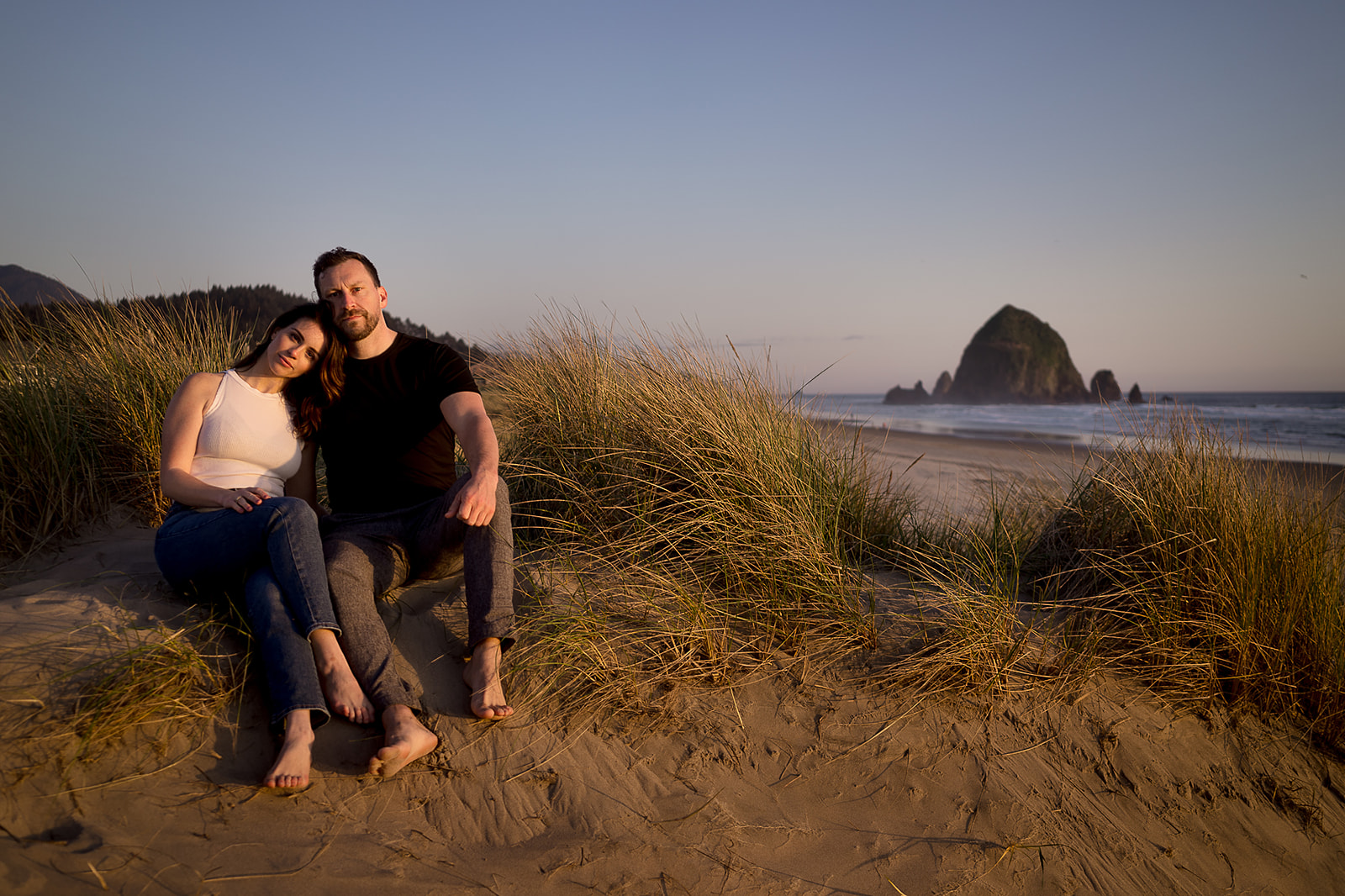 couple leans into each other with haystack rock behind them during Cannon Beach Engagement session