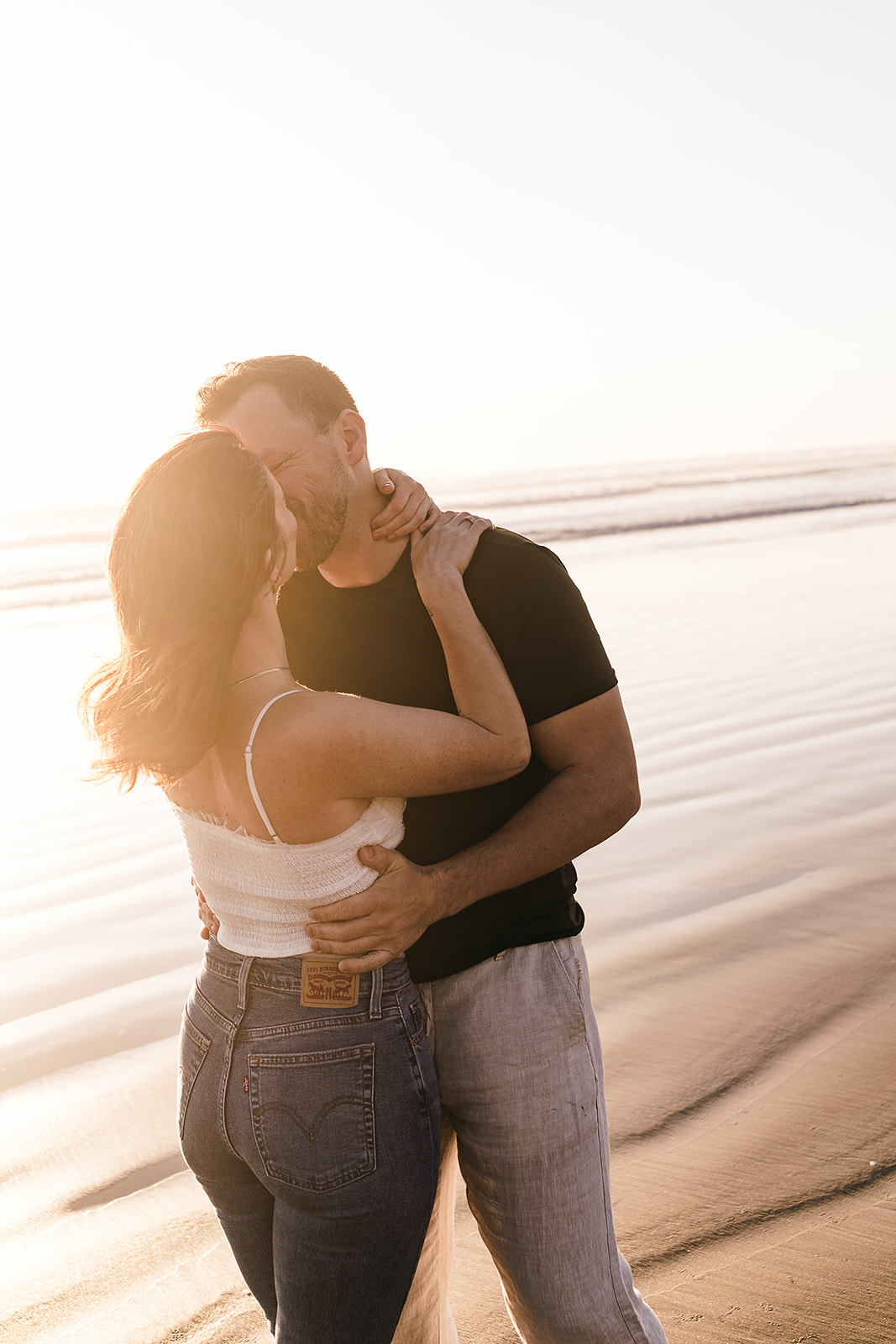 couple sneaks a kiss during cannon beach engagement session