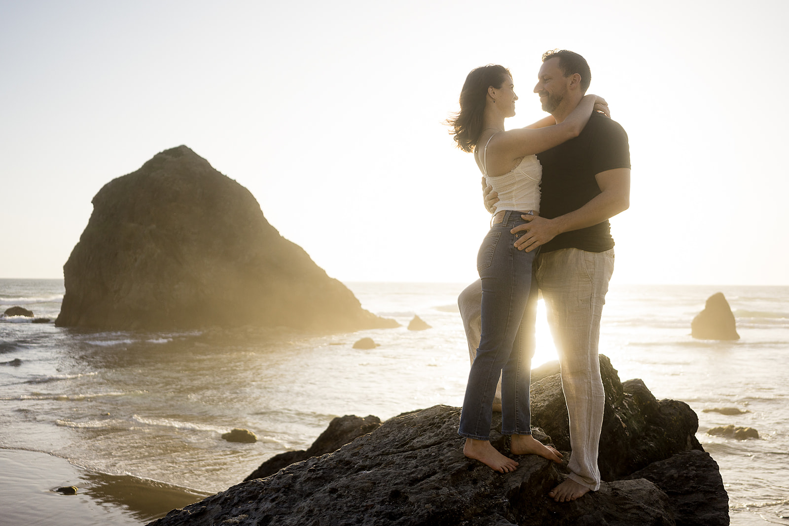 couples stands in front of the sunset at hidden beach during their Cannon Beach Engagement session