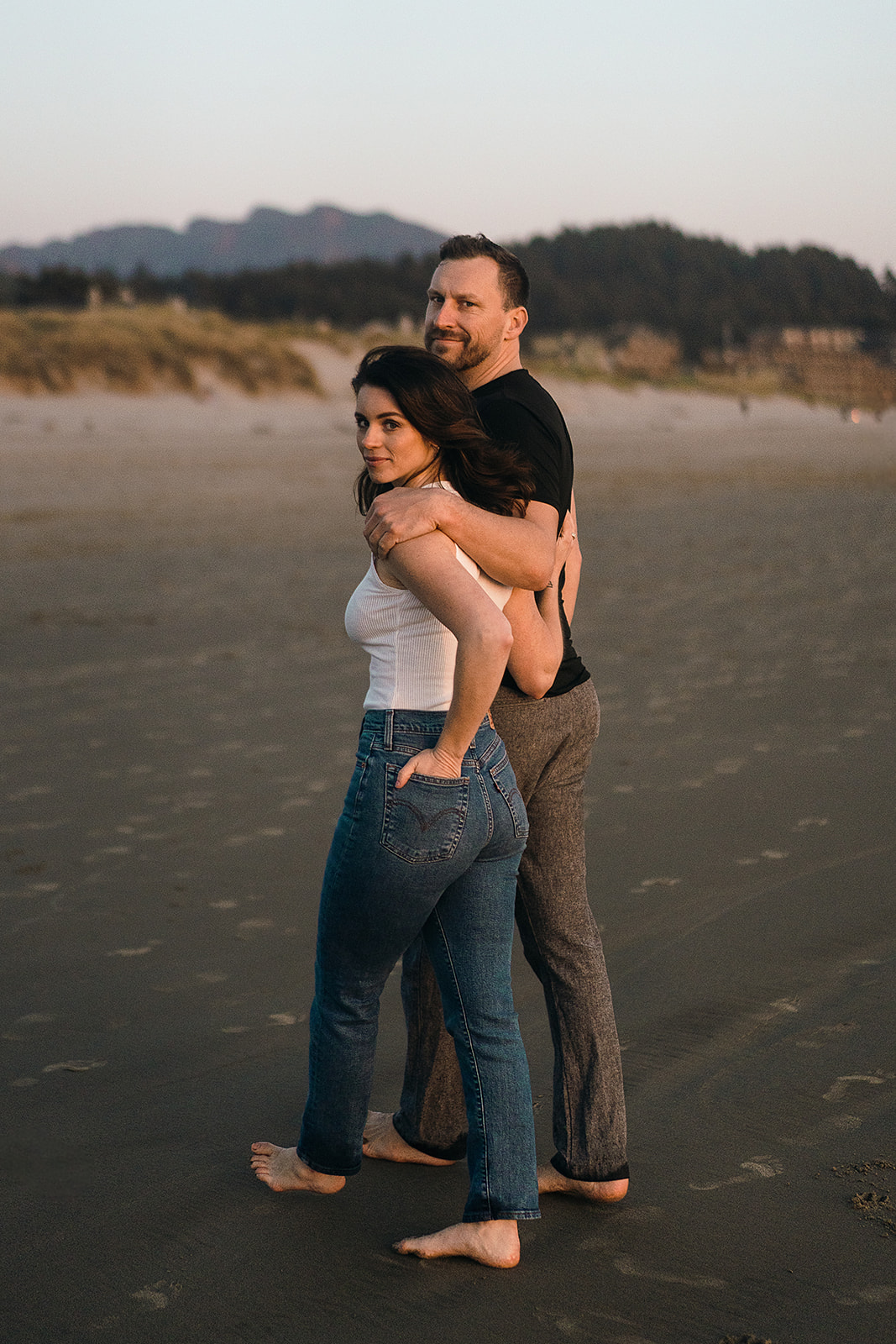 couples looks back at the camera while walking on the beach during Cannon Beach Engagement session