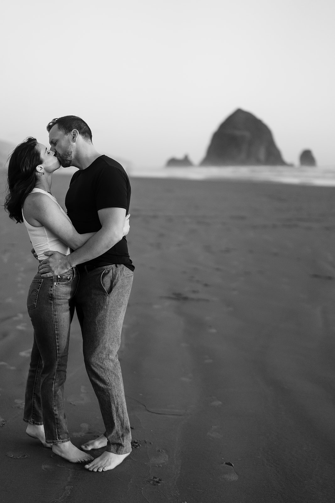 couple kisses during sunset with haystack rock behind them for their Cannon Beach Engagement session