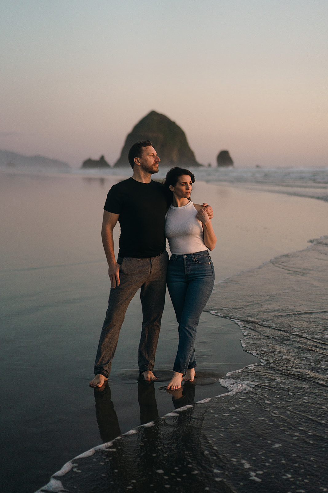 couples watches sunset on the Oregon Coast during their Cannon Beach Engagement session