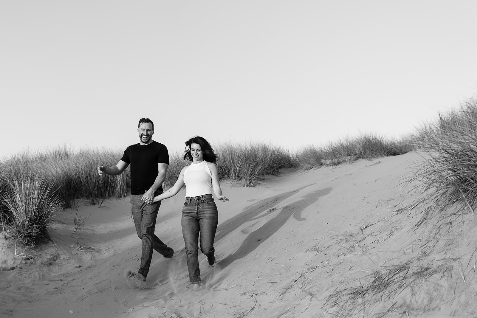 couple runs down sand dunes on the Oregon Coast at Cannon Beach Engagement session