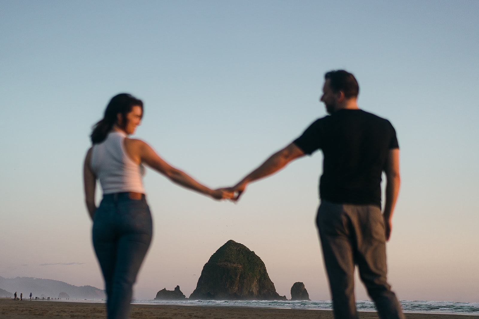 Couple holds hands over Haystack Rock during their Cannon Beach Engagement session