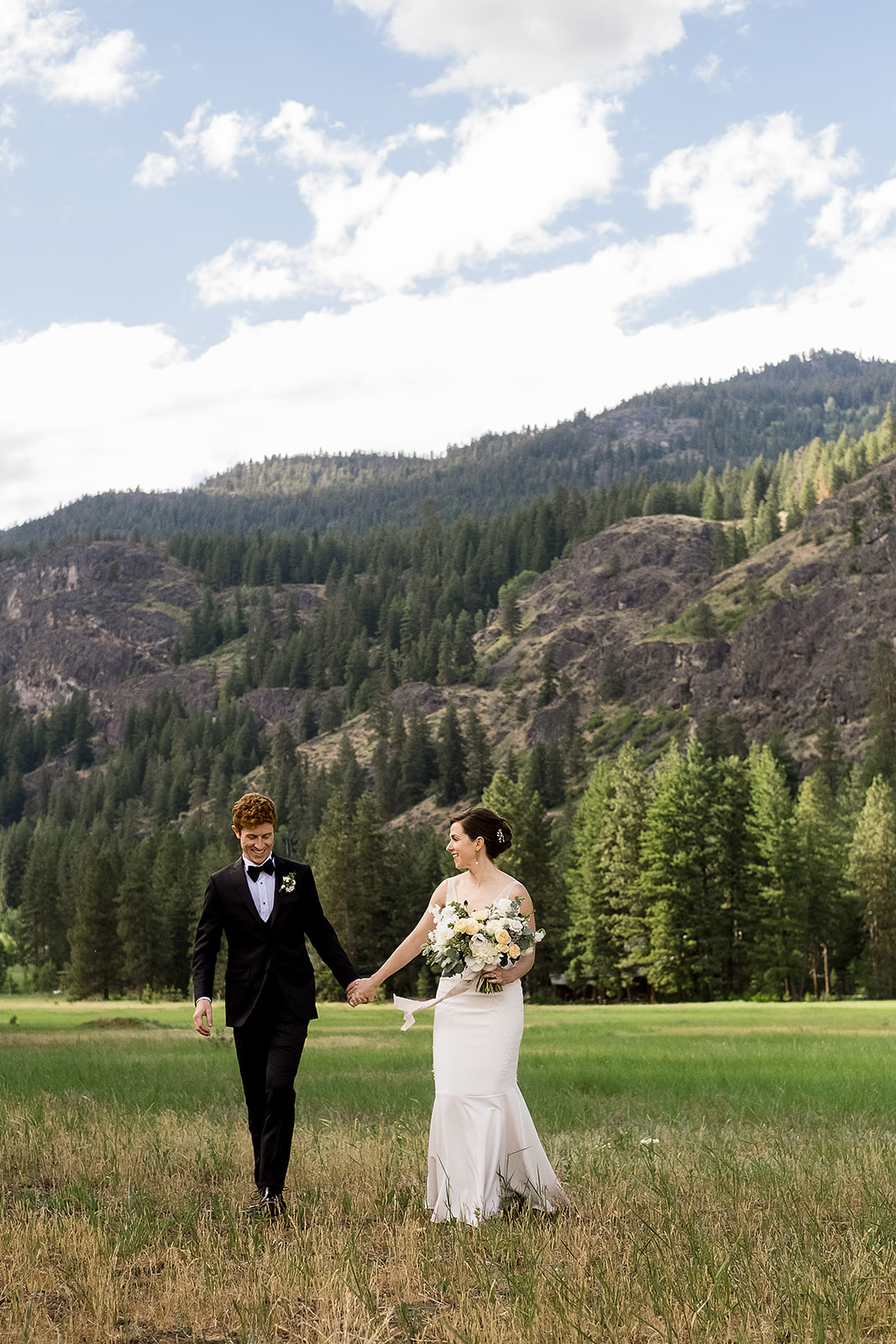 bride and groom walk through field in Methow Valley during their Mazama Ranch House wedding
