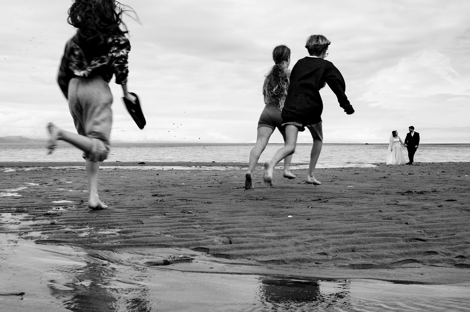 BW photo of a bride and groom on the beach in Comox and kids running by