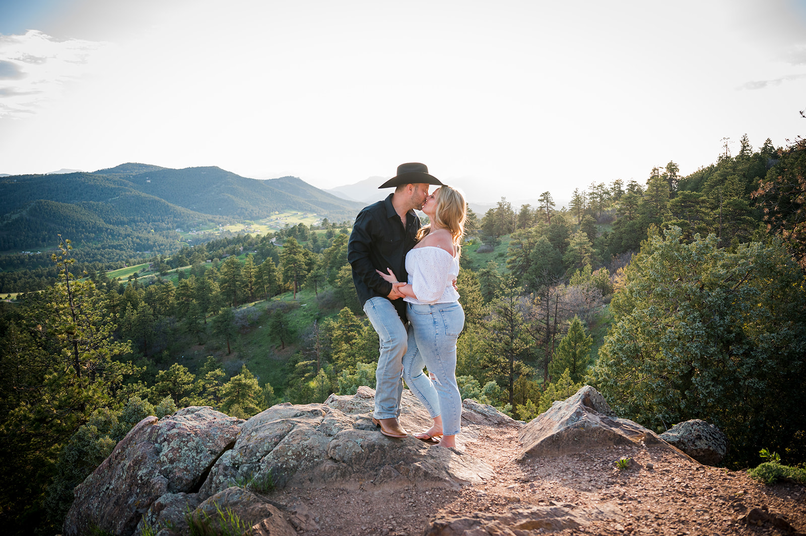 Couple shares a kiss atop Upper Mount Falcon with Colorado valley views in the background.