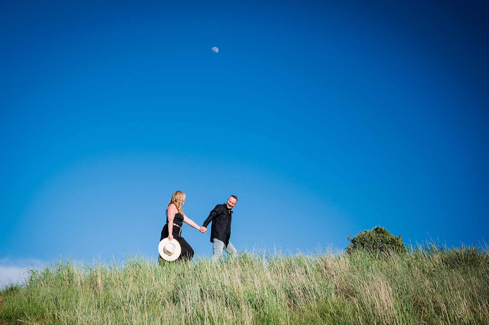 Man leads woman by the hand across open field with a big blue sky in the background.