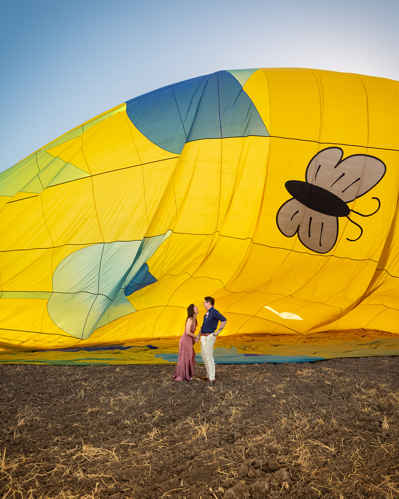 nonbinary person proposing to their girlfriend in front of yellow hot air balloon