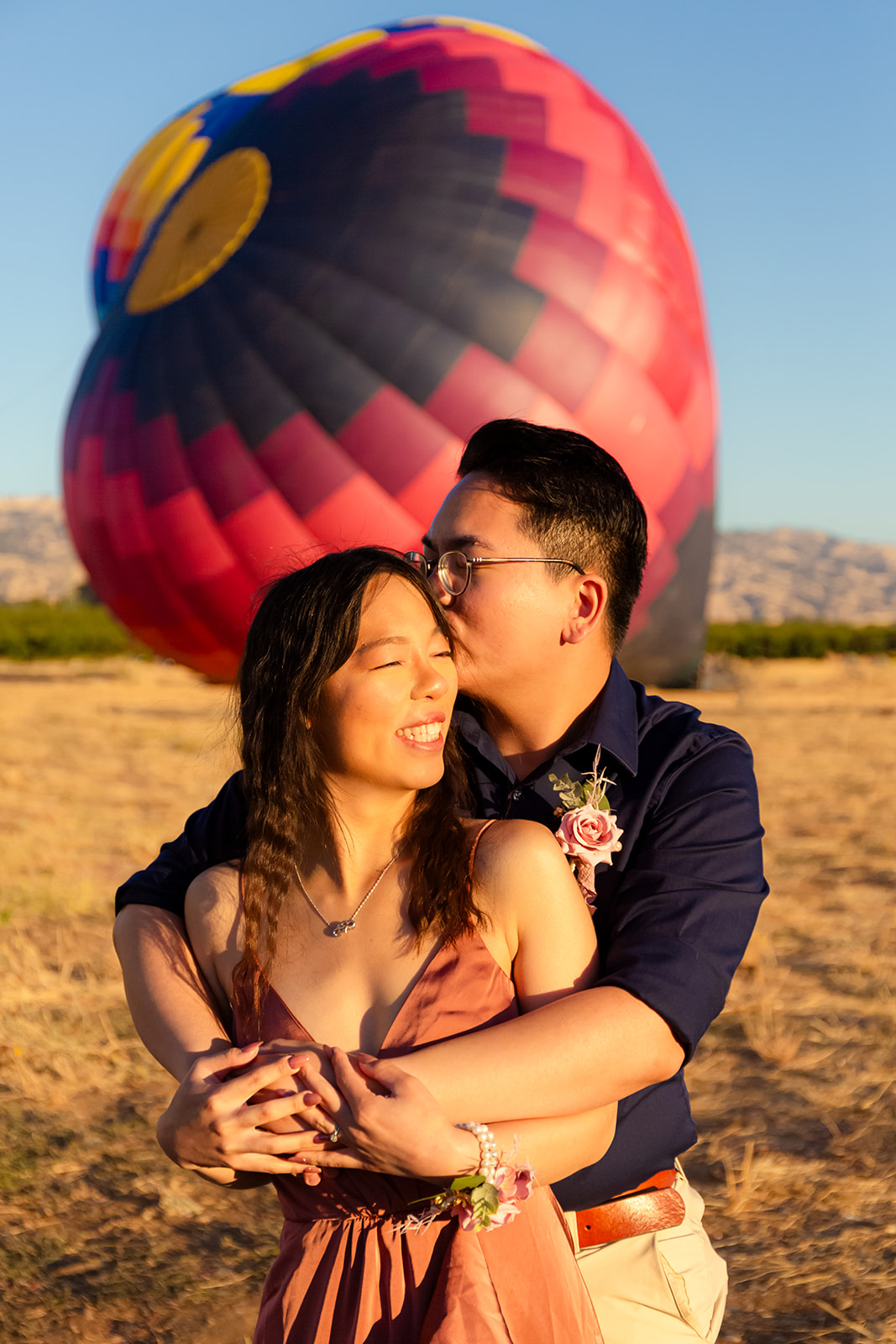 nonbinary person and their girlfriend embracing in front of colorful hot air balloons