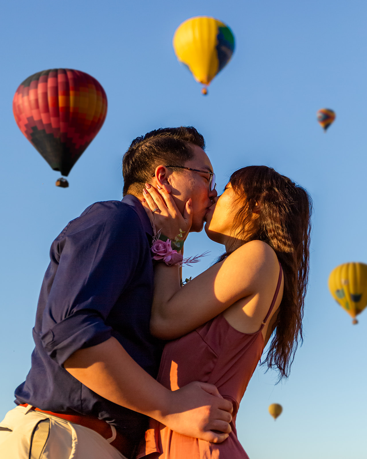 nonbinary person and their girlfriend kissing in front of colorful hot air balloons